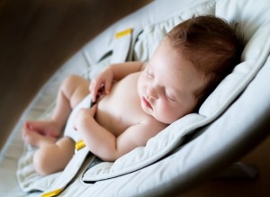 Sweet newborn baby girl sleeping in a bouncer chair in a dark ro