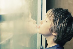 Cute 6 years old boy looking through the window